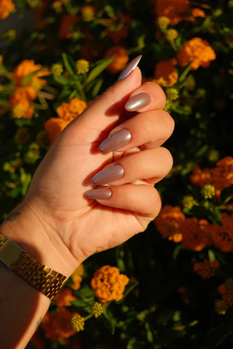 Mano con uñas almendradas color topo sosteniendo flores naranjas