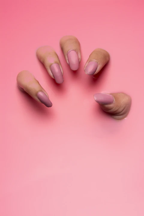 Mano con uñas en rosa malva sobre fondo rosado